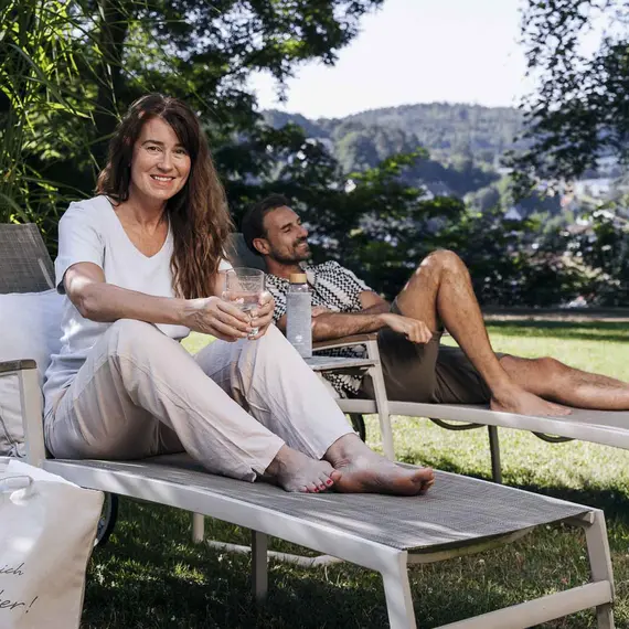 Eine Frau und ein Mann sitzen auf zwei Liegen umgeben von Natur