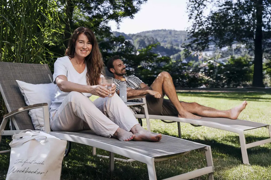 Eine Frau und ein Mann sitzen auf zwei Liegen umgeben von Natur